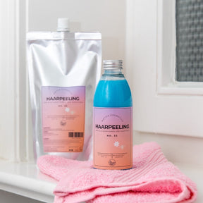 Moodbild Haarpeeling Set, Shampoo im Vordergrund auf Rosa Handtuch